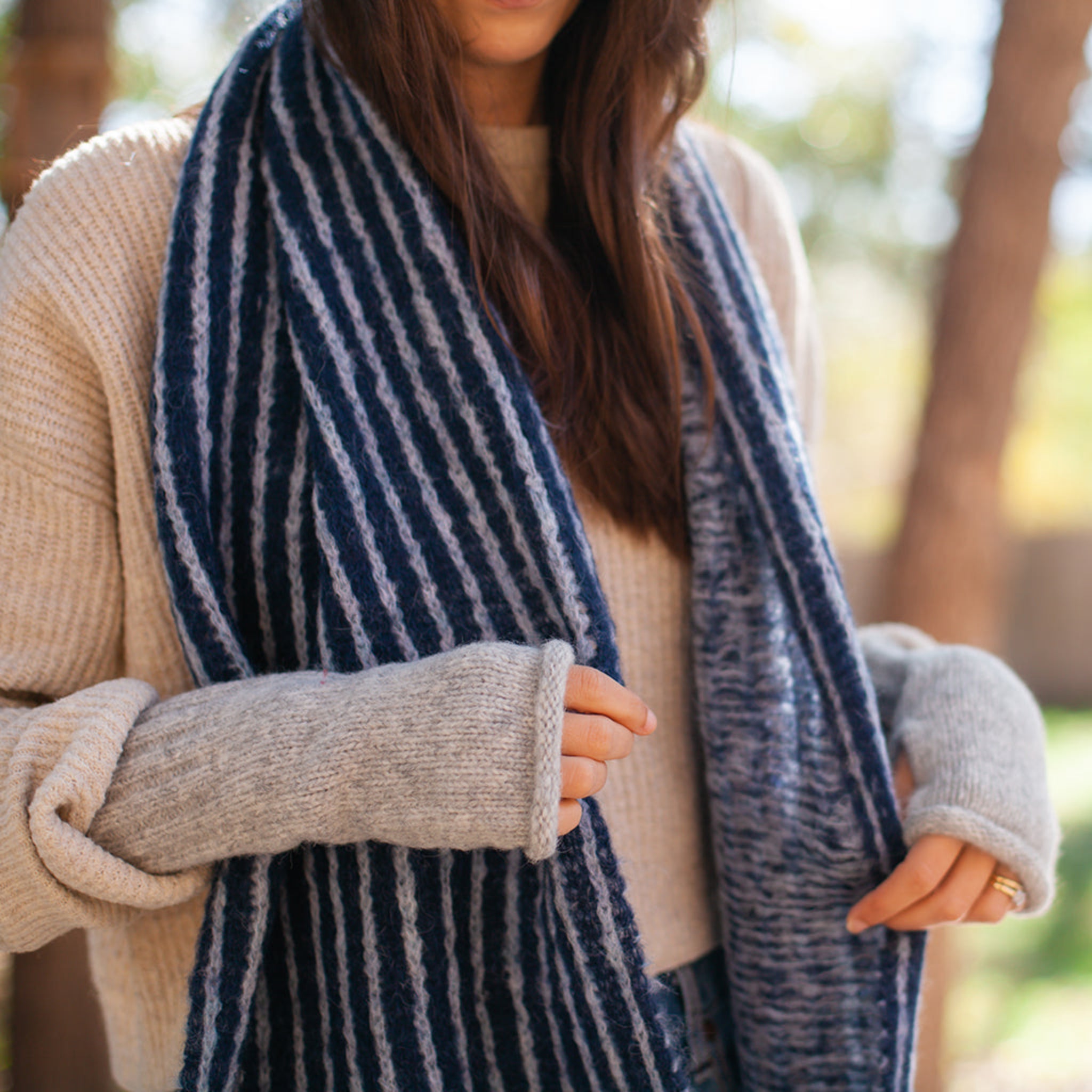 Person wearing a blue and white striped alpaca scarf with a blurred outdoor background