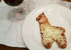 Pizza shaped like a dog on a white plate with a glass of red wine in the background.