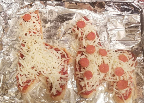 Two pizza-shaped bread slices with cheese and pepperoni on a piece of tinfoil.