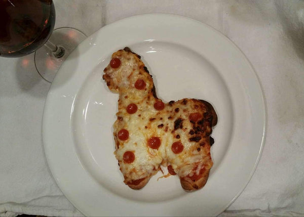 Alpaca-shaped pizza on a white plate with a glass of red wine in the background.