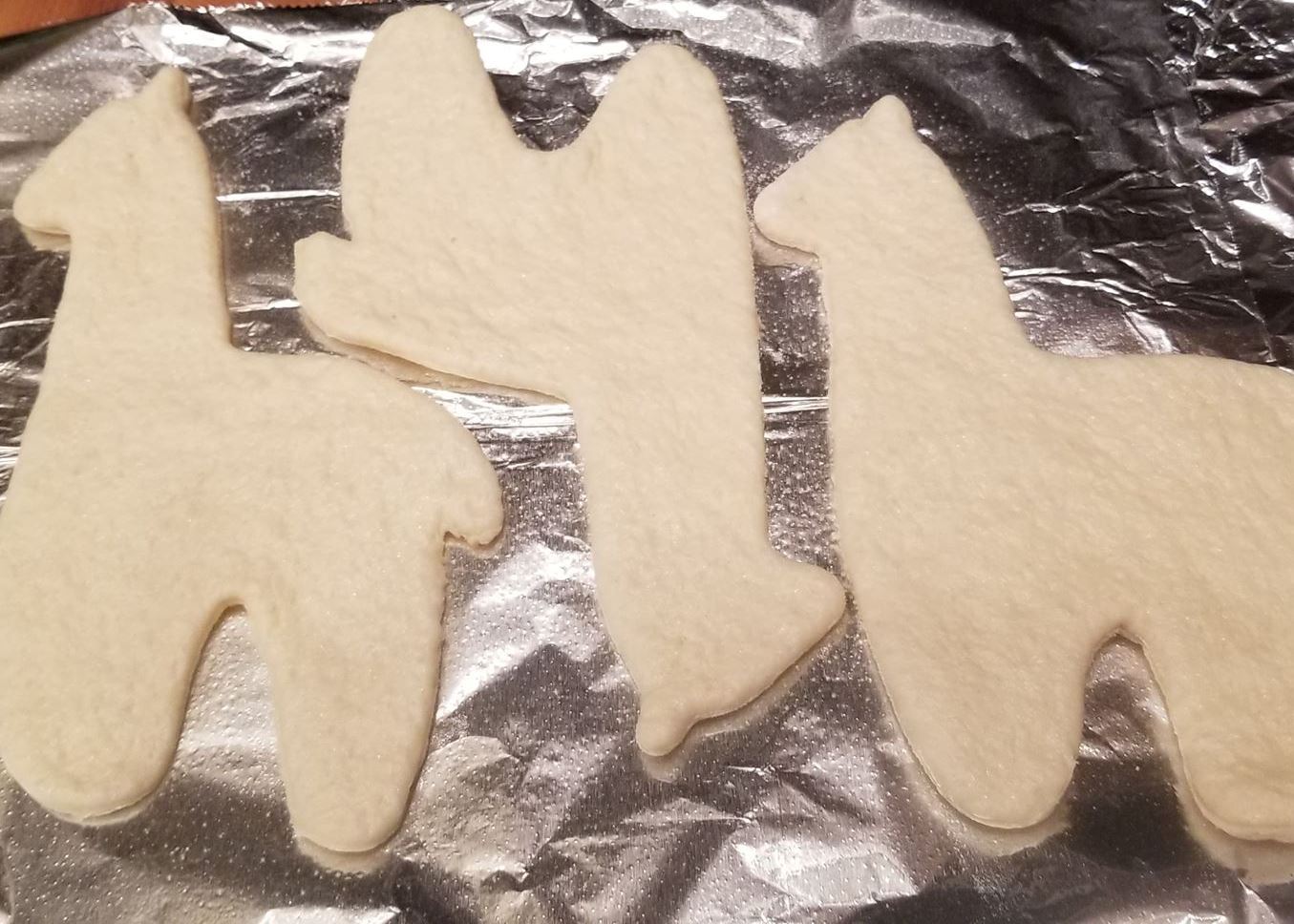 Unbaked cookie cutouts shaped like animals on a baking sheet with tinfoil.