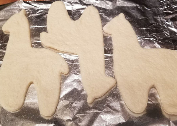 Unbaked cookie cutouts shaped like animals on a baking sheet with tinfoil.