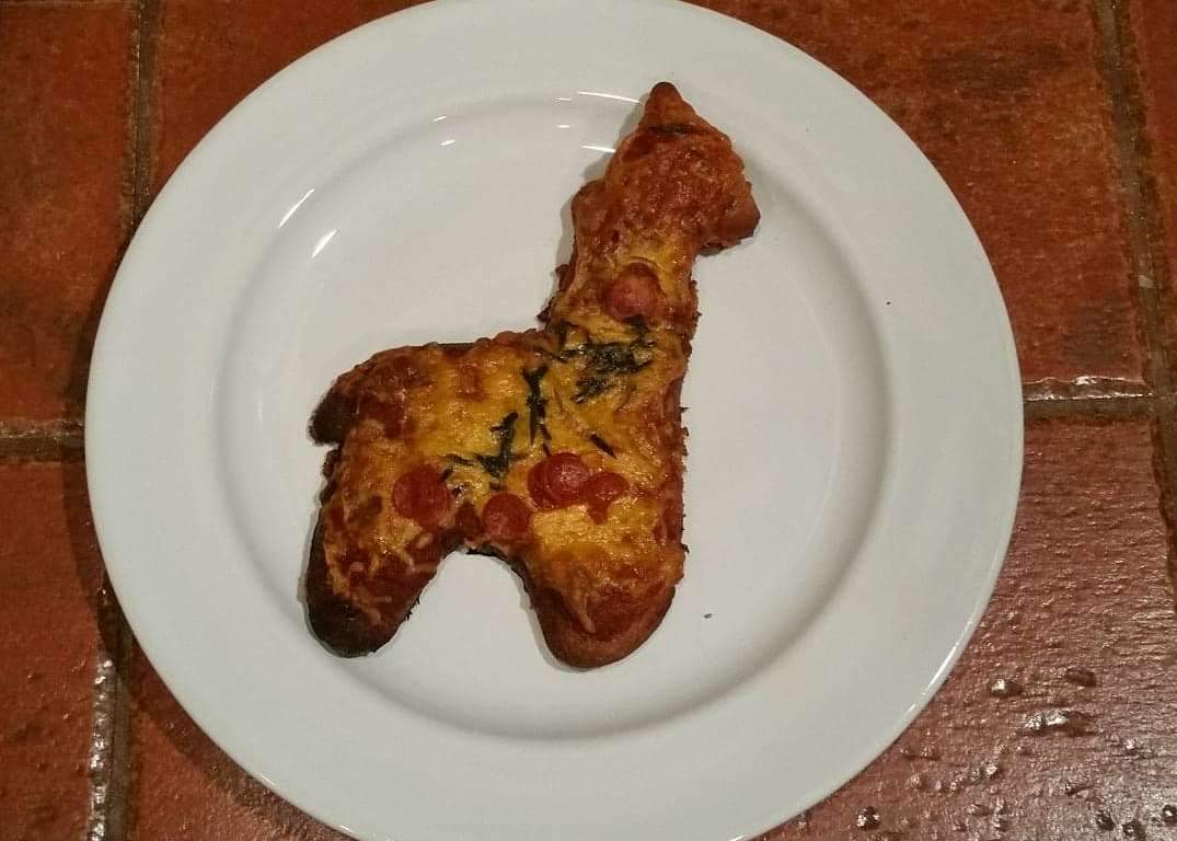 Pizza shaped like a dog on a white plate with a red brick background