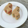 Two bear-shaped sandwiches on a white plate with a wooden background