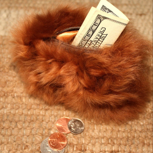 Brown fur pouch with money and coins on a textured surface