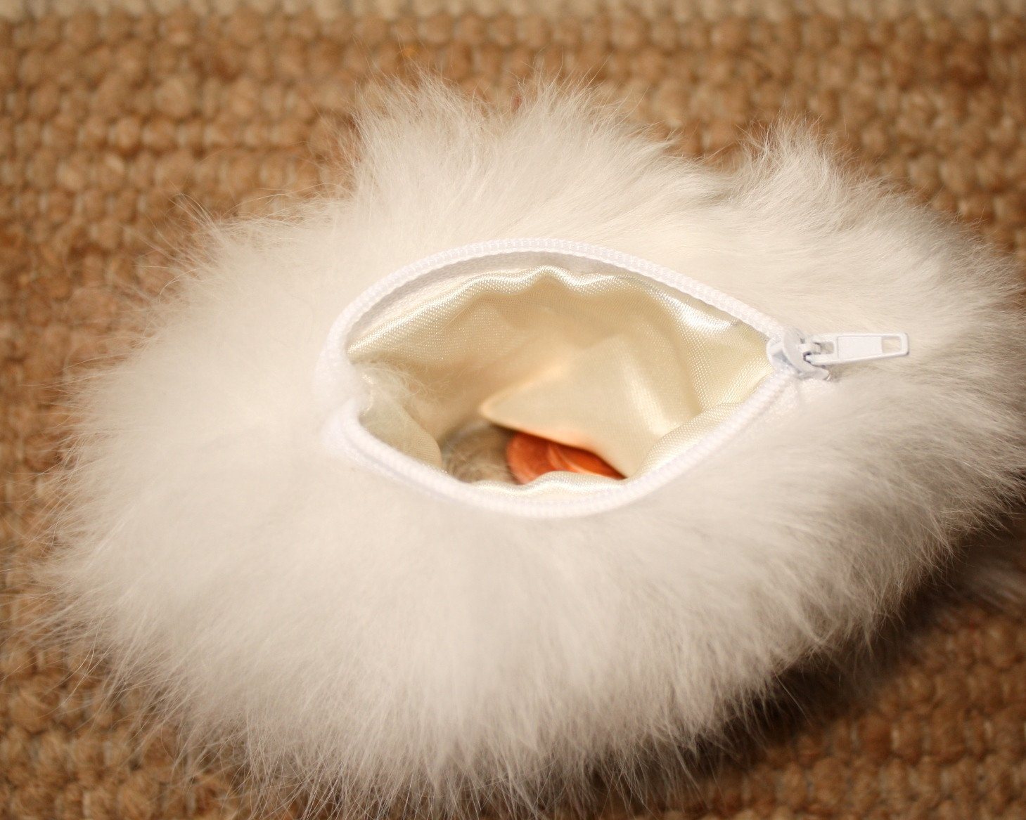 White fur pouch with a zipper on a beige carpet