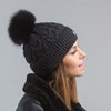 Woman wearing a black knit beanie with a pom-pom on a gray background
