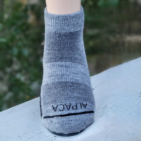 Gray alpaca sock on a mannequin foot with a blurred green background
