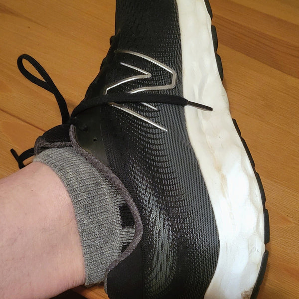 Black athletic shoe with white sole worn by a person on a wooden floor