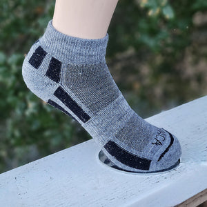 Purely Alpaca grey golf sport sock worn on foot, low-show ankle style, standing on wooden surface with green background