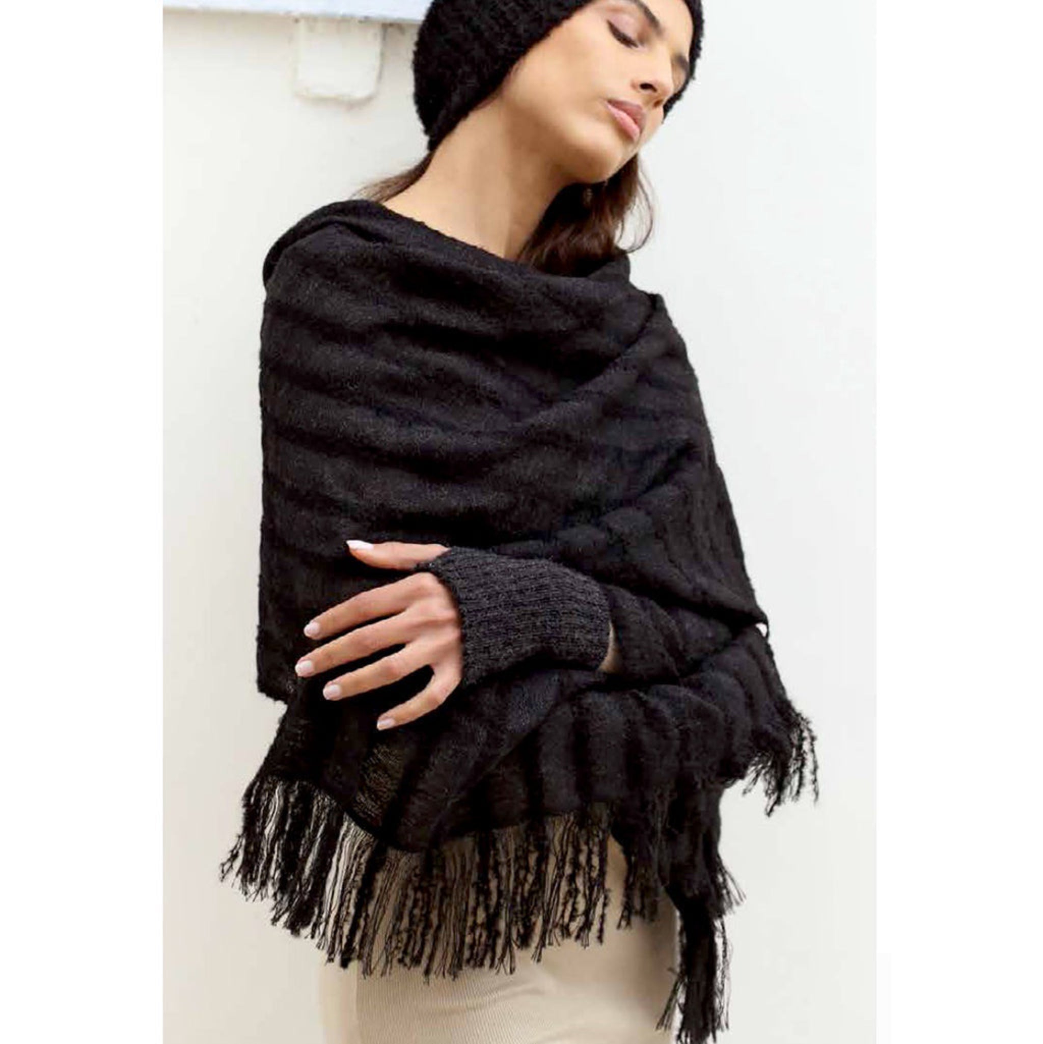 Woman wearing a black fringed alpaca scarf and beanie against a white background