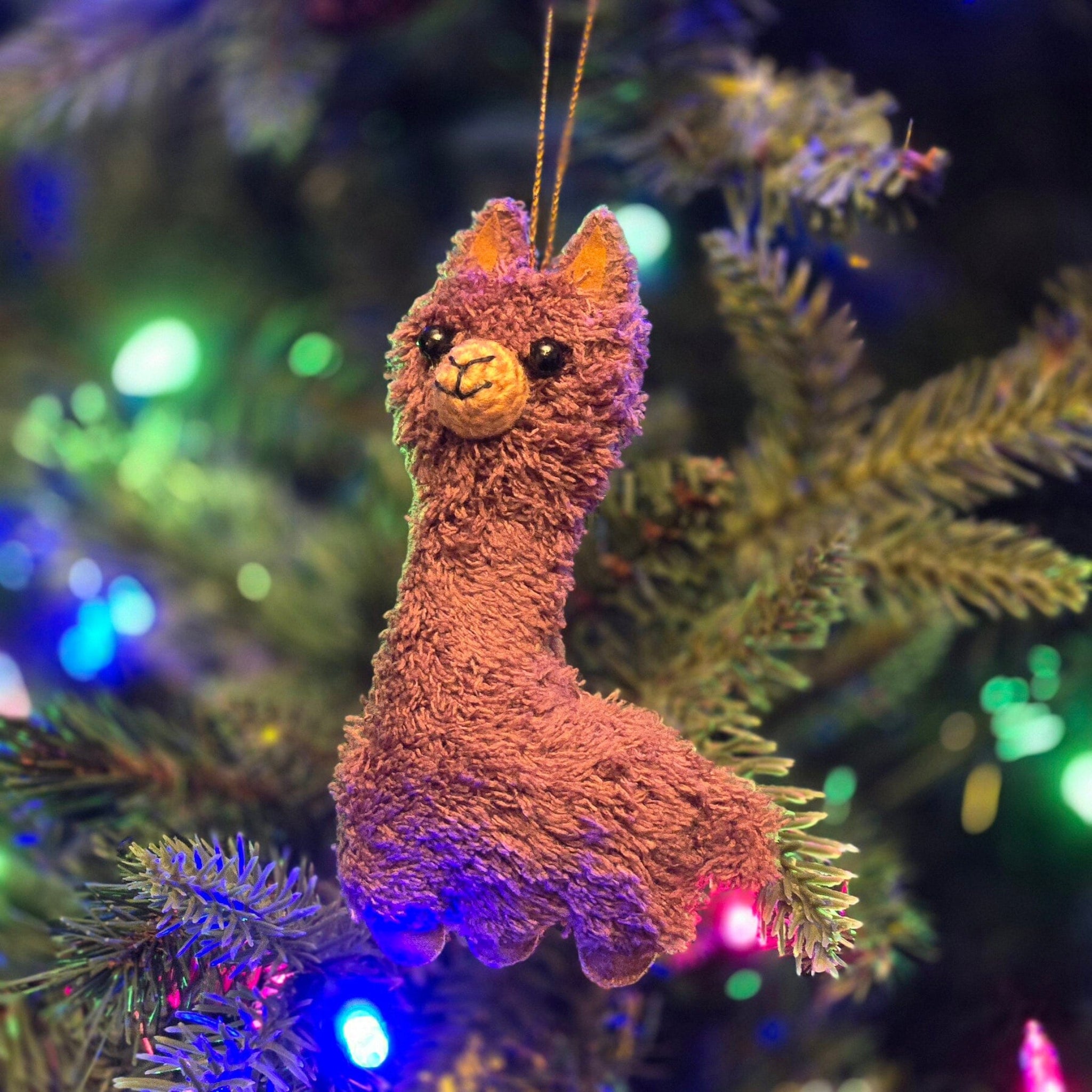 Plush llama ornament on a decorated Christmas tree with colorful lights.