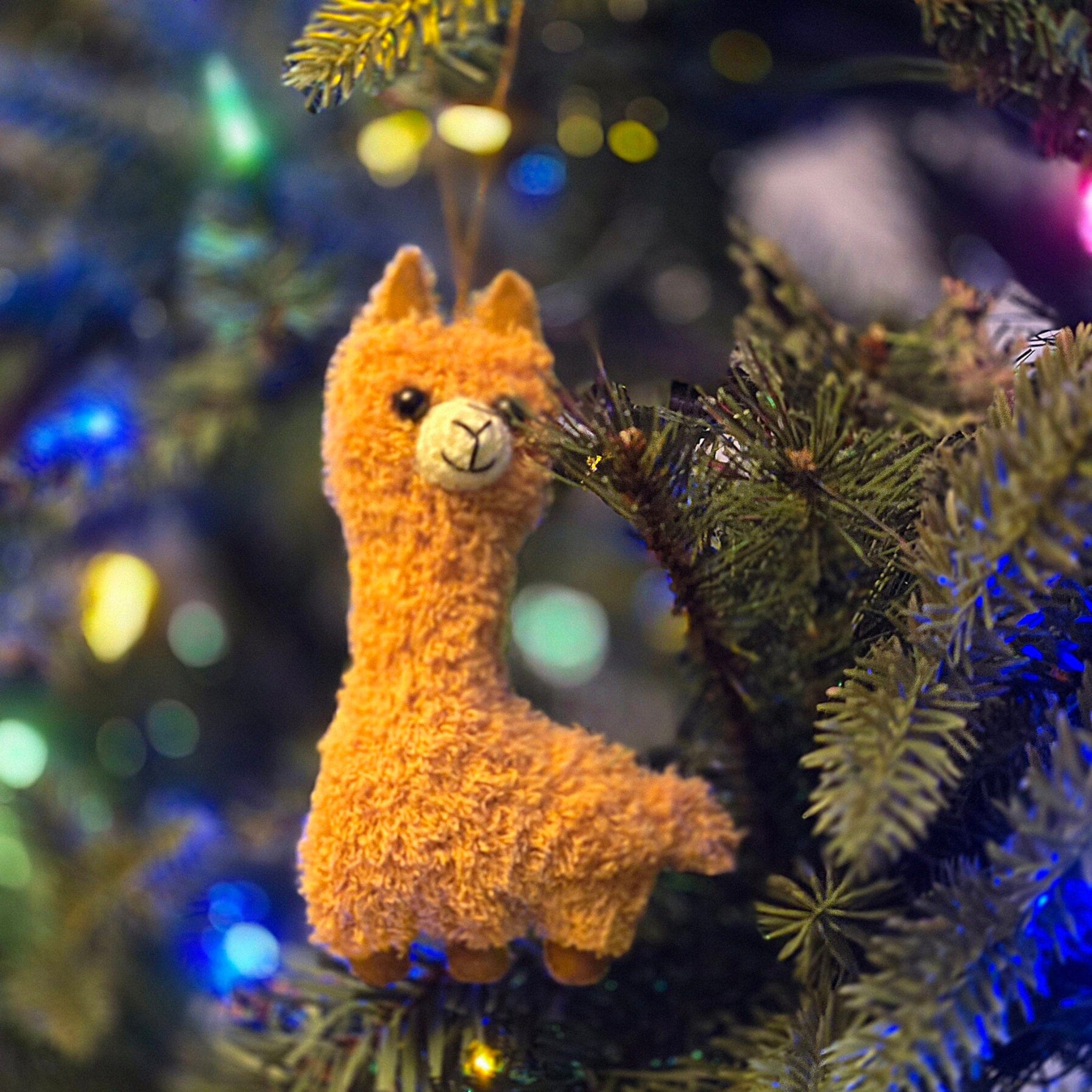Plush llama toy hanging on a decorated Christmas tree with blurred lights in the background