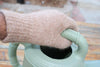 Hand wearing a beige glove holding a green watering can.