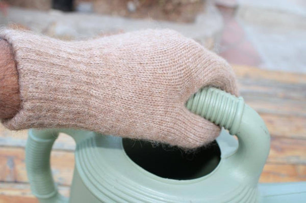 Hand wearing a beige glove holding a green watering can.