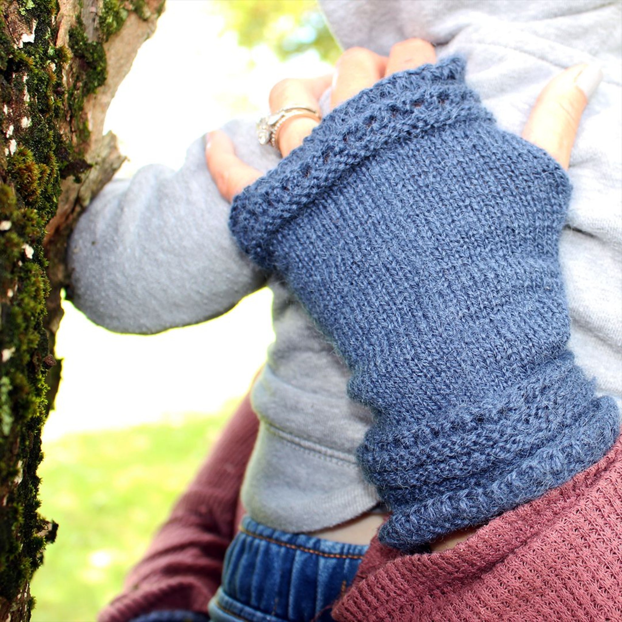 Person wearing blue knitted fingerless gloves in a natural setting