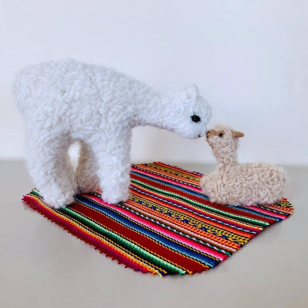 Two plush toys, a white bear and a beige lamb, on a colorful woven mat against a white background.