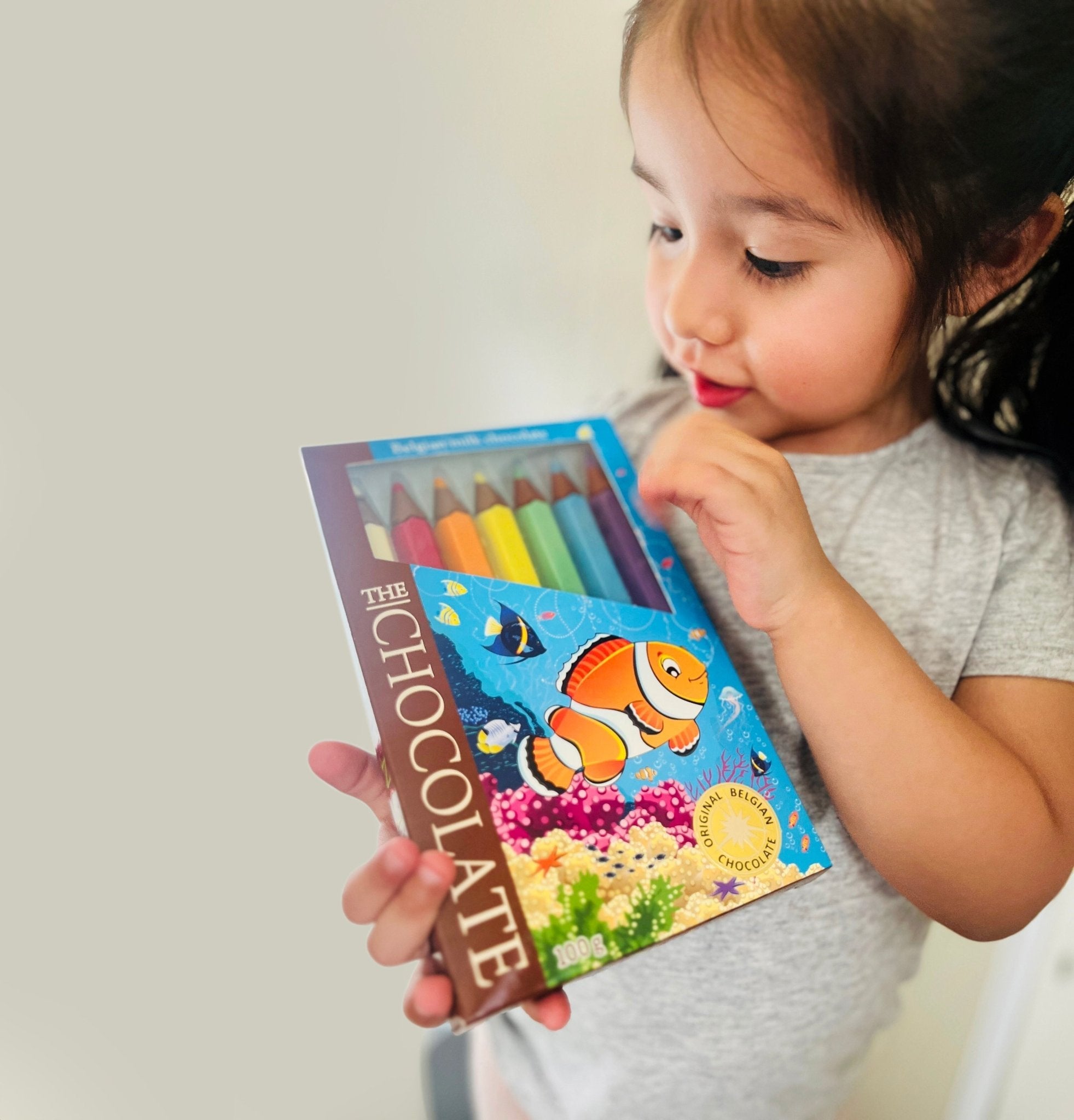 Child holding a colorful book with a fish illustration on a plain background