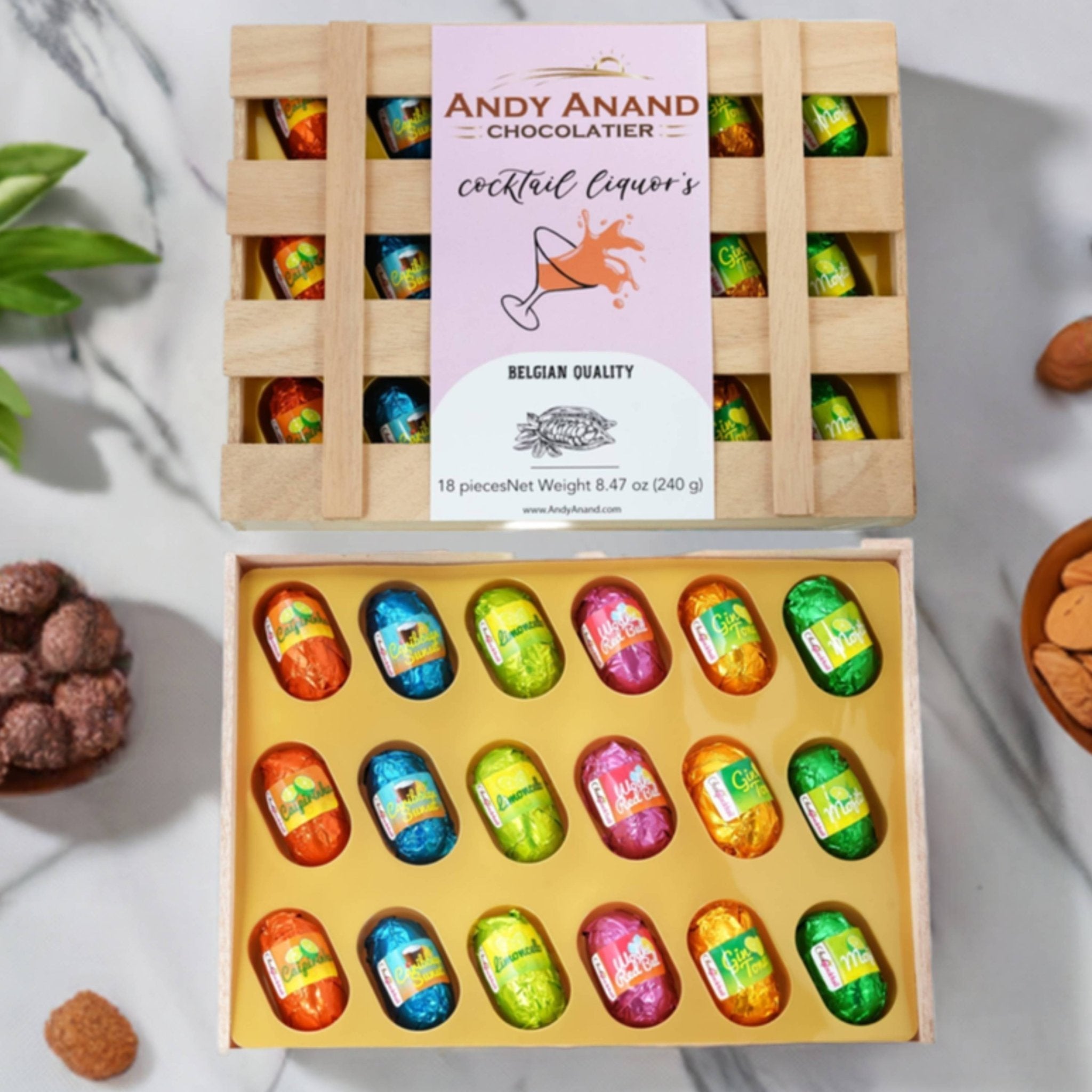 Box of Andy Anand Chocolatier cocktail liquors with a wooden crate on a light background.