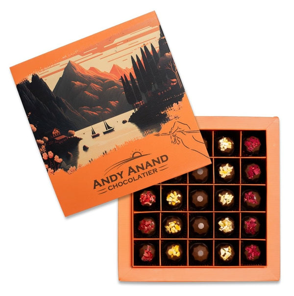 Chocolates in an open box with a scenic design on the lid, featuring the brand 'Andy Anand Chocolatier'.