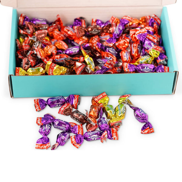 Box of colorful wrapped candies with some spilling out onto a white surface.