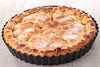 Apple pie in a black tart pan on a light wooden surface