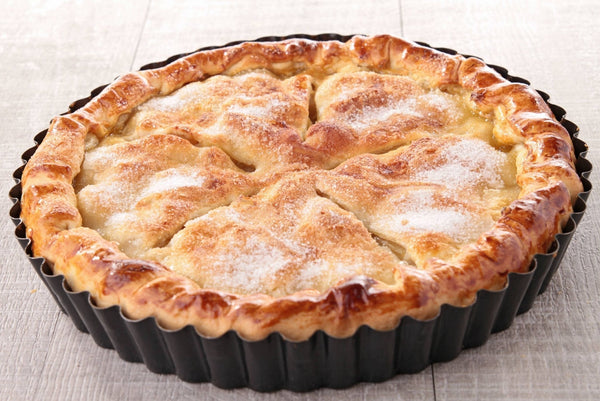 Apple pie in a black tart pan on a light wooden surface