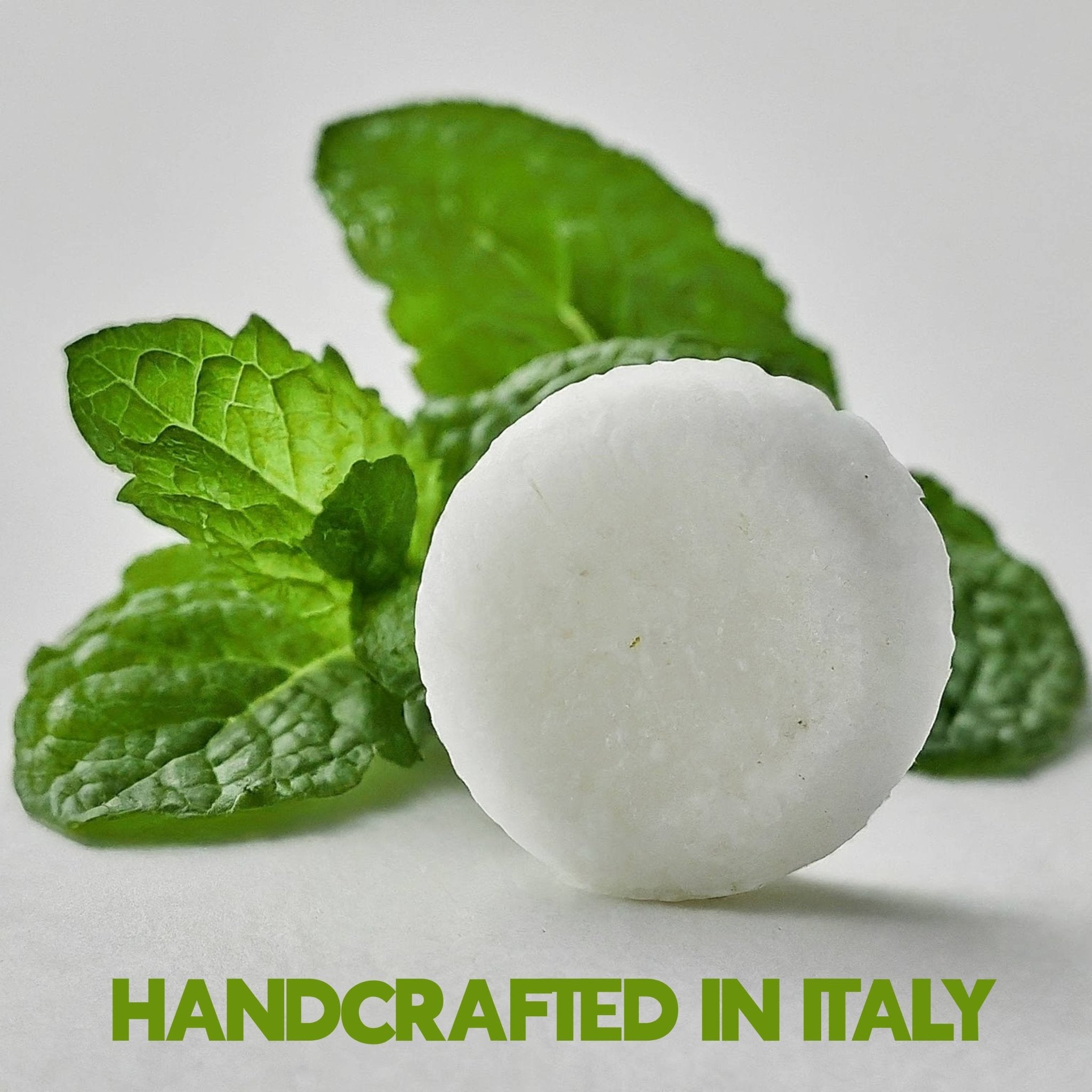 White spherical bath bomb with green leaves on a light background, labeled 'Handcrafted in Italy'.