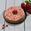 Round cake with pink crumb topping and raspberries on a white wooden surface with red roses.