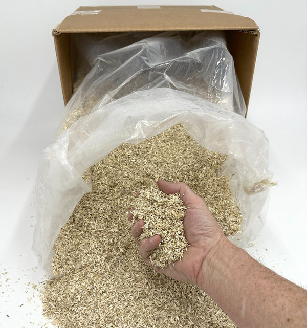 Hand holding a handful of wood chips next to an open cardboard box with a plastic bag inside.