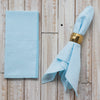 Light blue napkin with a gold napkin ring on a wooden surface