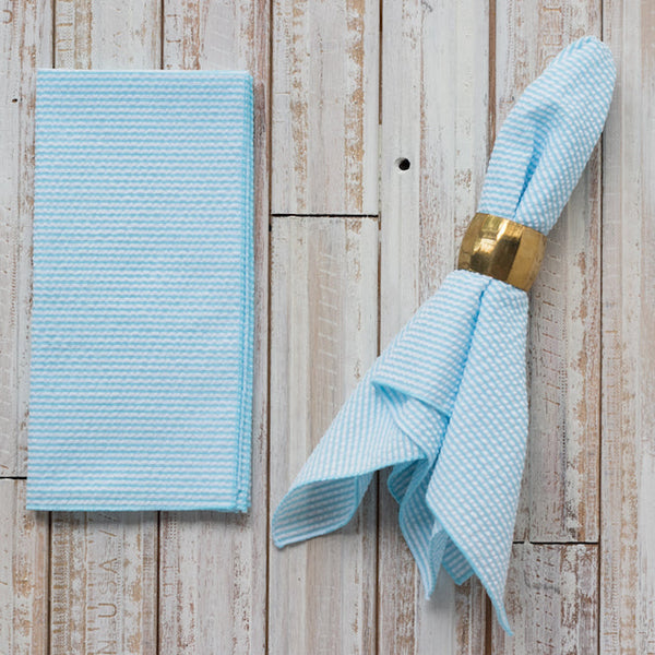 Light blue napkin with a gold napkin ring on a wooden surface
