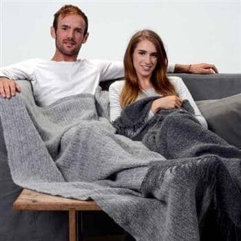 Man and woman sitting on a couch under a gray blanket with a light gray background