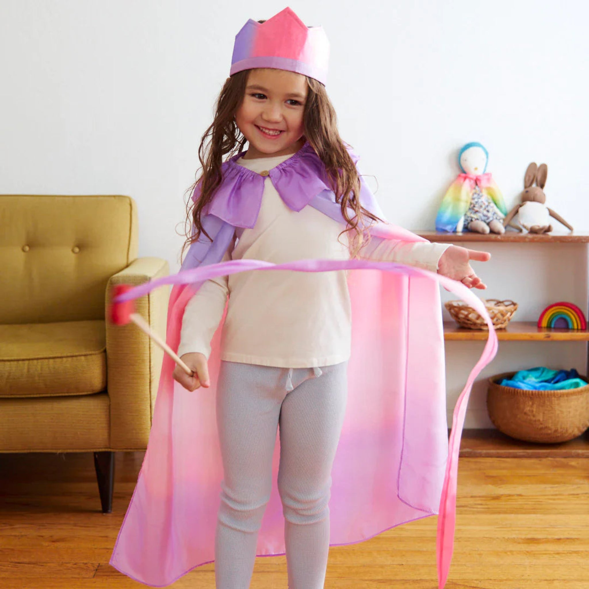 Child in a pink and purple costume with a rainbow-colored toy in the background