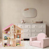 Wooden dollhouse with pink roof and chair in a room with a dresser and mirror.