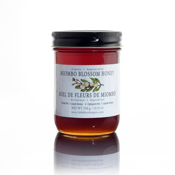 Jar of Miombo Blossom Honey with a label on a white background. Experience pure, raw honey with Organic Miombo Blossom Honey. Sourced from African wilderness bees, this Fair Trade and USDA Organic product has a unique butterscotch flavor.