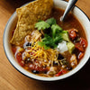  bowl of chili with tortilla chips, cilantro, sour cream, and avocado on a wooden table