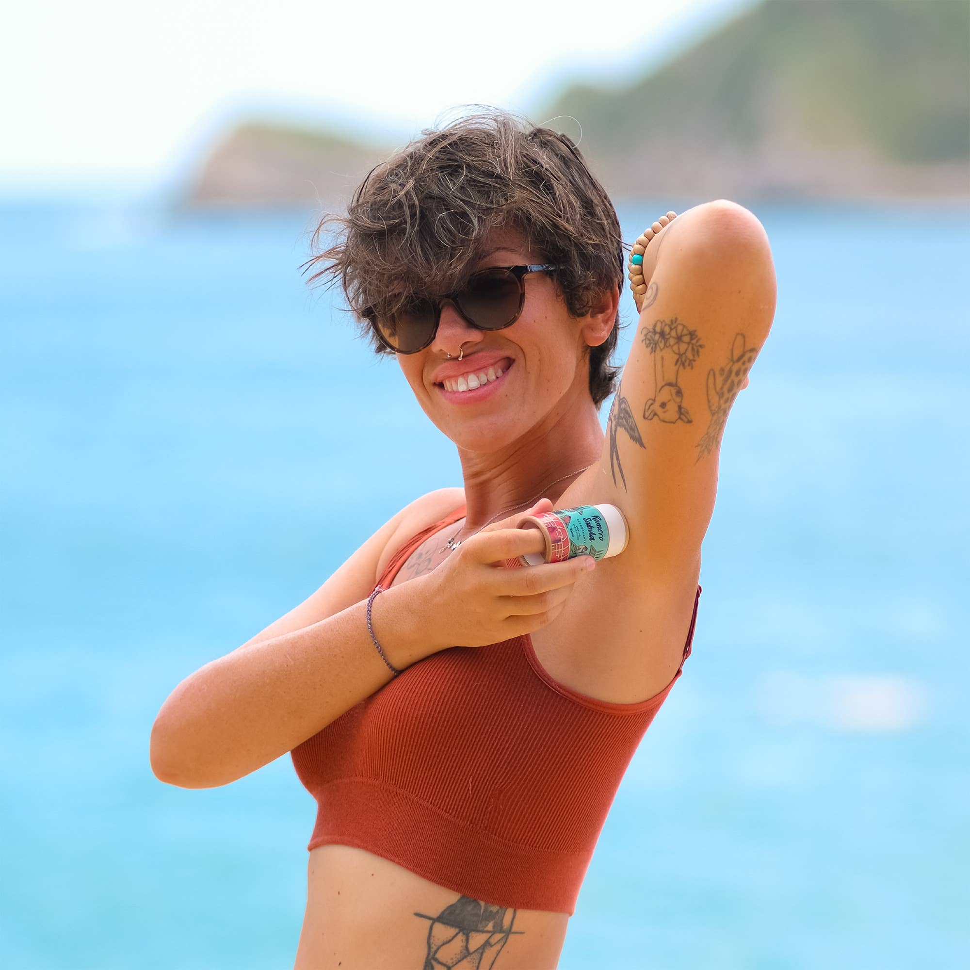Woman applying sunscreen on a beach with a clear blue sky and ocean in the background. Natural Pitahaya Deodorant — Aluminum-Free Solid Deodorant with Magnesium & Dragon Fruit | 24-Hour Protection, Plastic-Free & Handmade
