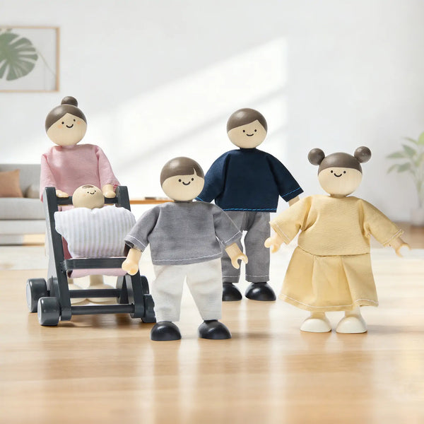 Four wooden toy children figures with fabric clothing and black feet, including a stroller figure, arranged on a light wood floor against a softly blurred indoor background.