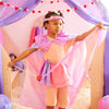 Young girl in a colorful dress playing inside a play tent with pink and purple accents.