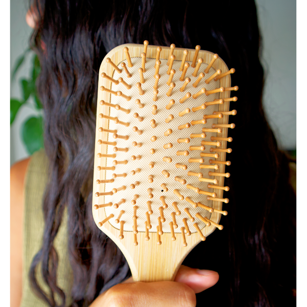 Wooden hairbrush held by a person with long dark hair.