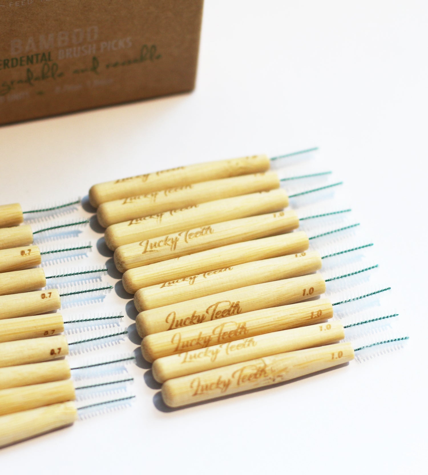 Bamboo dental brush picks with 'Lucky Teeth' branding on a striped cloth, with a cardboard box in the background.