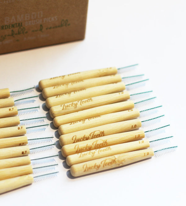 Bamboo dental brush picks with 'Lucky Teeth' branding on a striped cloth, with a cardboard box in the background.