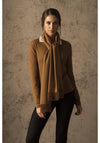 Woman wearing a brown sweater and scarf against a textured wall.