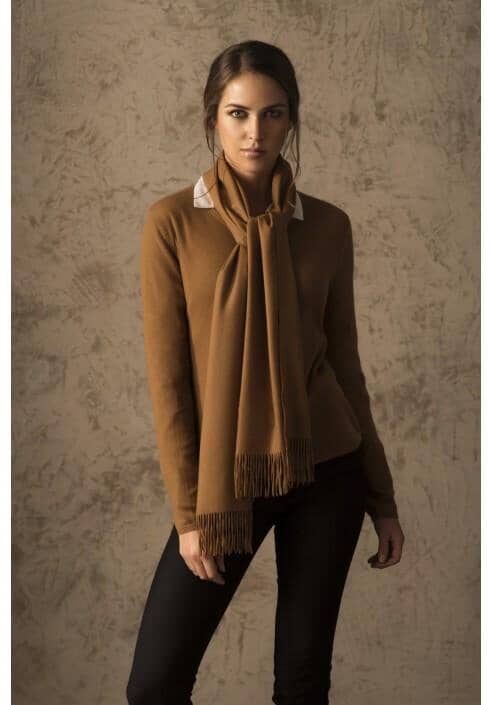 Woman wearing a brown sweater and scarf against a textured wall.