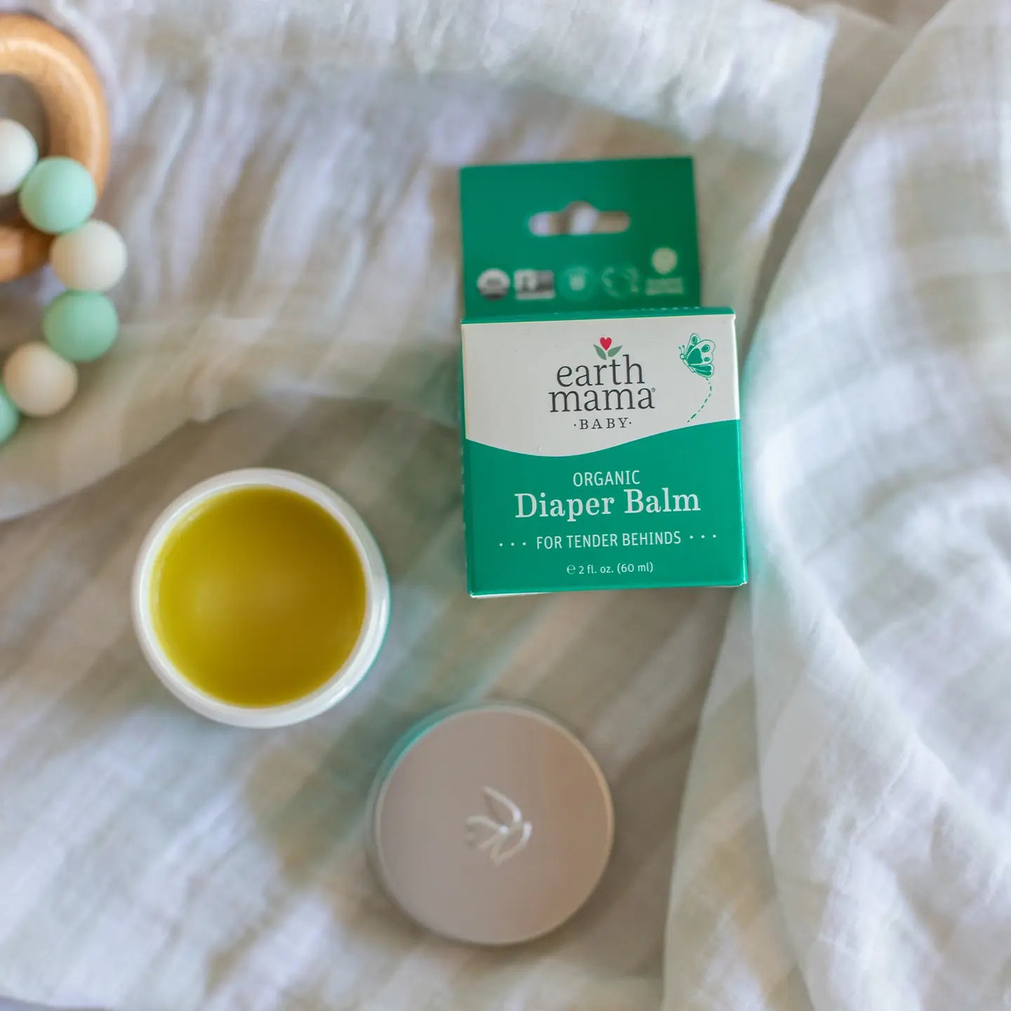 Earth Mama Organic Diaper Balm with container and packaging on a white fabric background