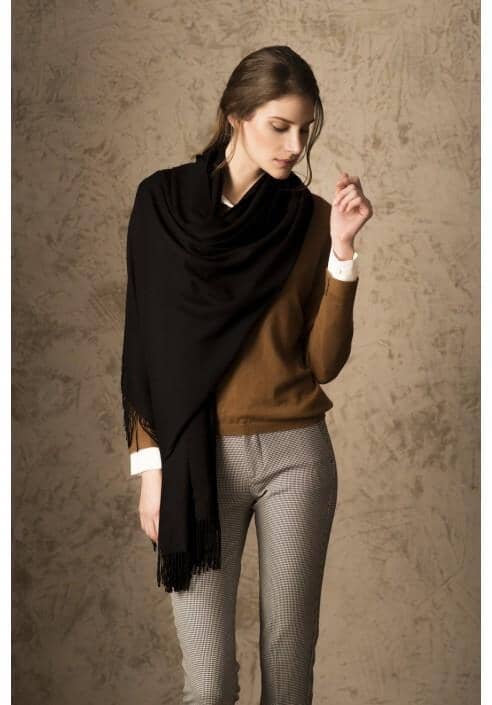 Woman wearing a black scarf, brown sweater, and gray pants against a beige background