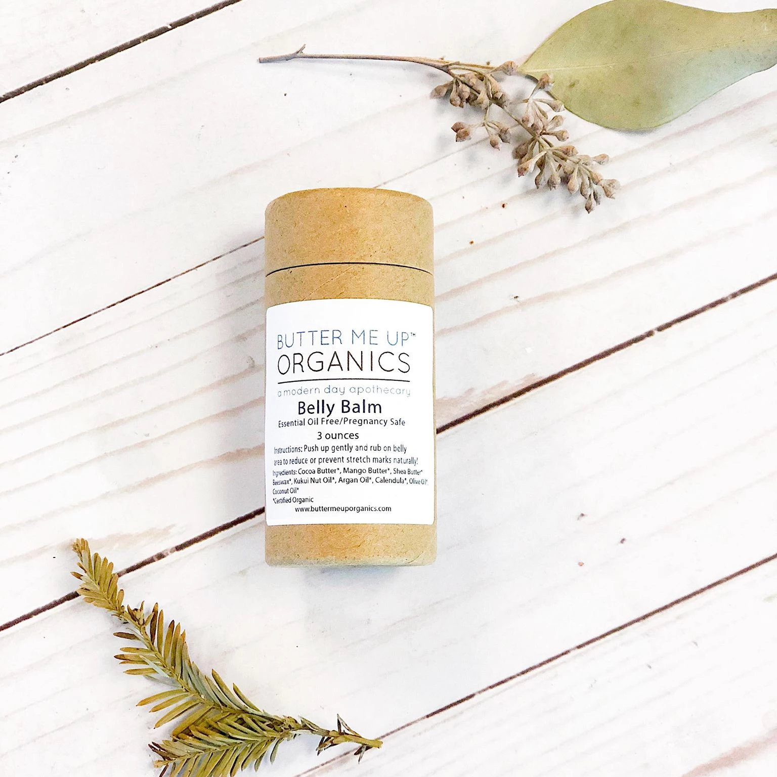 Butter Me Up Organics belly balm on a wooden surface with eucalyptus leaves.