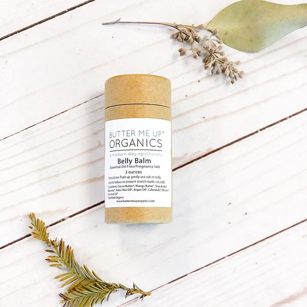 Butter Me Up Organics belly balm on a wooden surface with eucalyptus leaves.