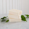 Three bars of soap stacked on a marble surface with green leaves.